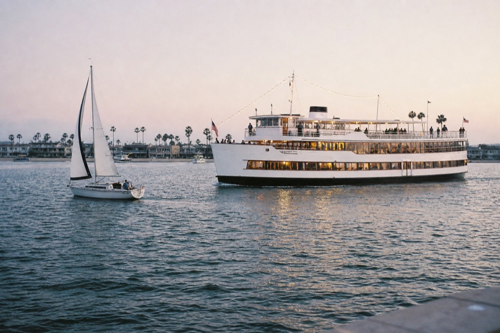 A lit dinner ship and a small sailboat on the bay at dusk, late-morning light