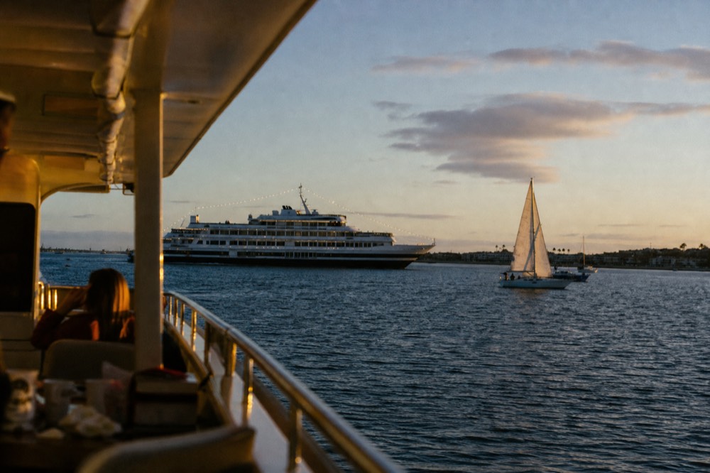 A lit dinner ship and a small sailboat on the bay at dusk at golden hour, long shadows and warm low light
