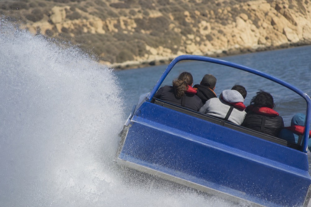 Jet boat leaning hard into a high-speed turn on San Diego Bay throwing a wall of spray as riders grip the rails