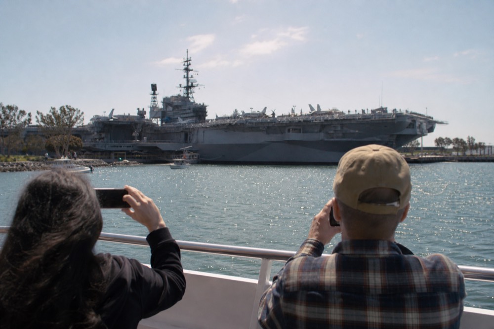 Passengers at the rail of a San Diego harbor cruise photographing the aircraft carrier museum across the water