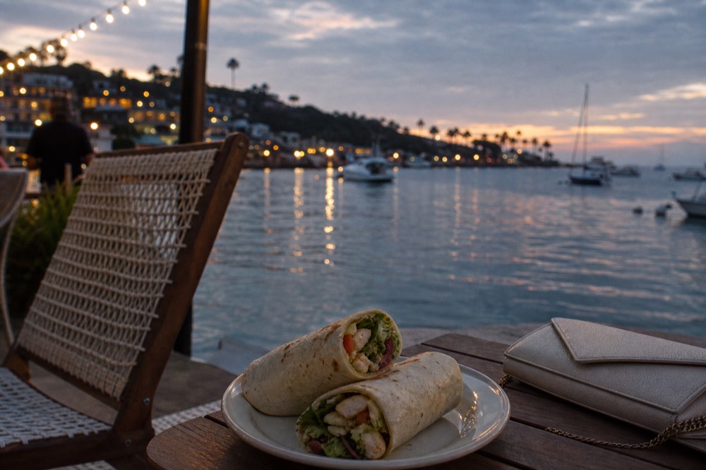 Wrap and clutch left on a deck chair at dusk on a San Diego sunset dinner cruise, string lights and water behind