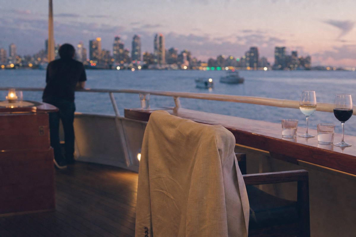 Couple in smart casual clothes with light jackets on the open deck of a boat at dusk