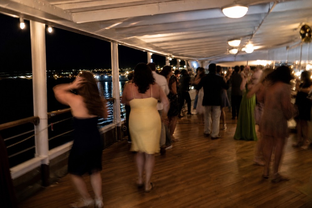 Dance floor on a San Diego dinner cruise lit warm at night with black bay water outside the windows