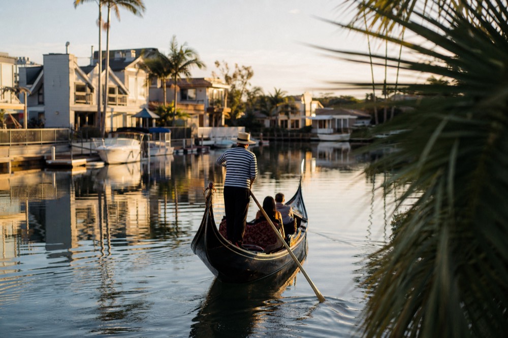 A black Venetian gondola in the calm canals of the Coronado Cays at golden hour, long shadows and warm low light